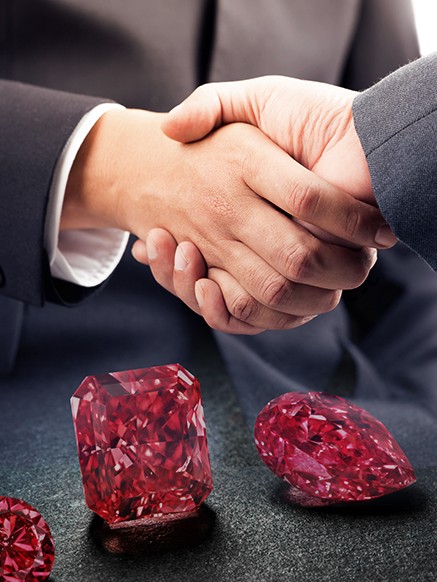 Two hands handshaking over a 3 pieces of diamond.