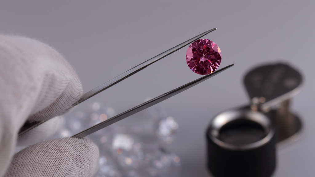 A pink diamond in tweezers.